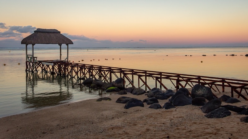 Sunrise over the lagoon and a thatched jetty at Bel Ombre beach on the south coast of Mauritius